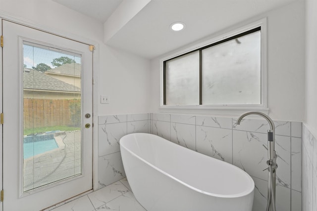 6711 Walton Heath Dr, Houston, TX 77069 - bathroom with tile walls, marble look tiles, a freestanding bath, a wainscoted wall, and recessed lighting