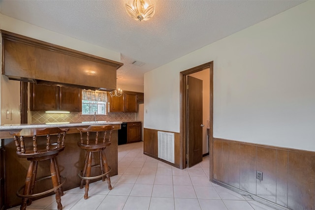 1015 Devonport Ln, Seabrook, TX 77586 - kitchen with a breakfast bar, decorative backsplash, a wainscoted wall, a textured ceiling, and light tile patterned flooring