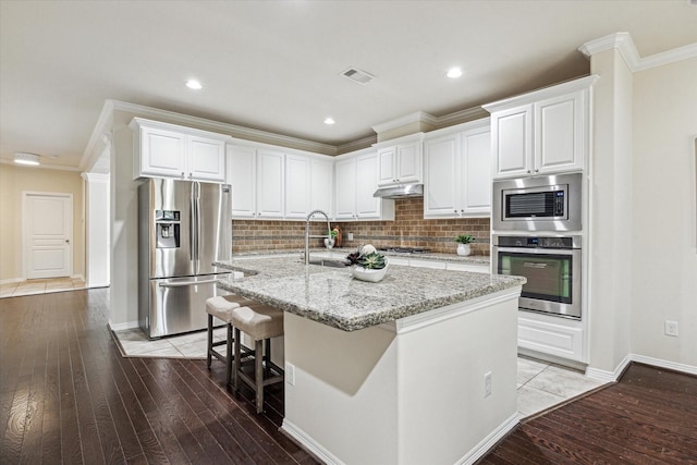 831 W 26th St, Houston, TX 77008 - kitchen featuring stainless steel appliances, ornamental molding, under cabinet range hood, white cabinets, and a center island with sink