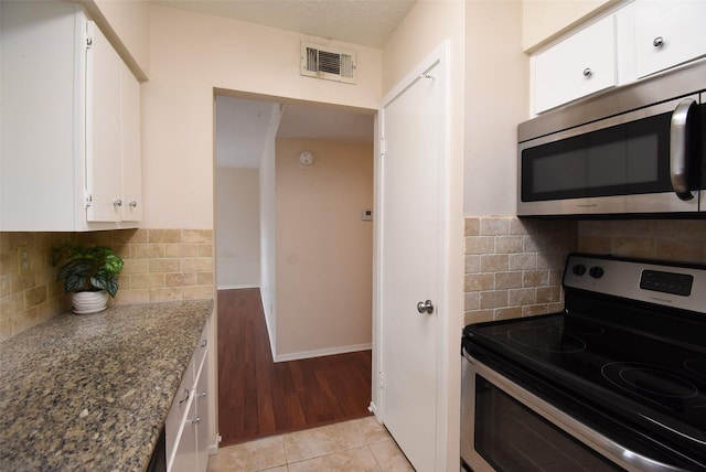 9007 Gaylord St Unit 23, Houston, TX 77024 - kitchen featuring appliances with stainless steel finishes, white cabinets, dark stone counters, backsplash, and light wood finished floors