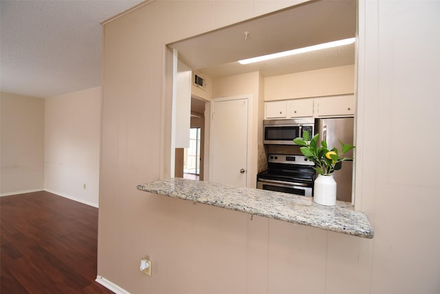9007 Gaylord St Unit 23, Houston, TX 77024 - kitchen with appliances with stainless steel finishes, dark wood-type flooring, a peninsula, white cabinets, and light stone counters