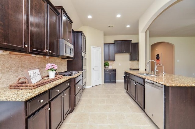 4327 Estes Ridge Ln, Katy, TX 77493 - kitchen featuring stainless steel appliances, arched walkways, tasteful backsplash, dark brown cabinets, and light stone counters