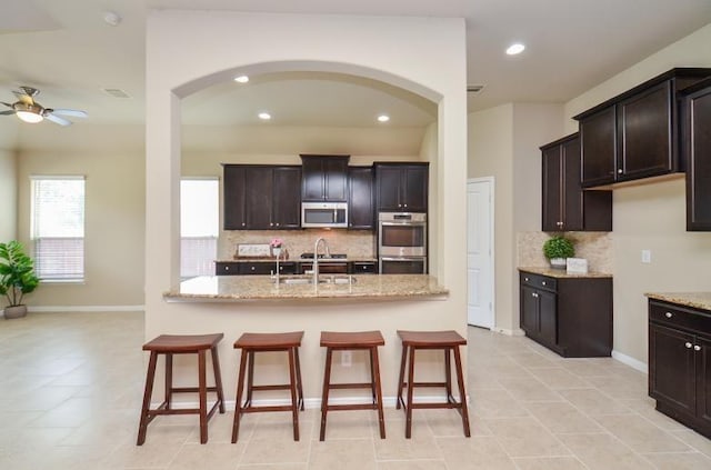 4327 Estes Ridge Ln, Katy, TX 77493 - kitchen with stainless steel appliances, a ceiling fan, arched walkways, light stone counters, and recessed lighting