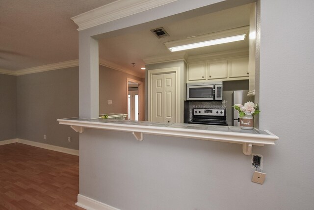 9005 Gaylord St Unit 19, Houston, TX 77024 - kitchen featuring appliances with stainless steel finishes, tile countertops, a kitchen bar, crown molding, and dark wood-type flooring