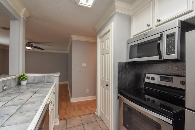 9005 Gaylord St Unit 19, Houston, TX 77024 - kitchen featuring appliances with stainless steel finishes, tile countertops, white cabinetry, crown molding, and light tile patterned flooring
