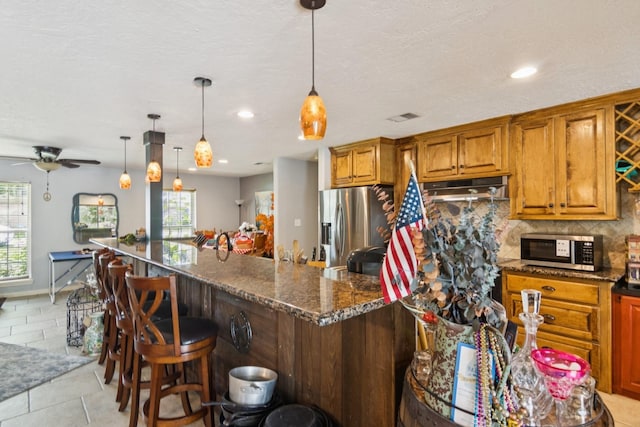 355 Cumberland Trl, Conroe, TX 77302 - kitchen featuring stainless steel appliances, a breakfast bar area, backsplash, brown cabinetry, and ceiling fan