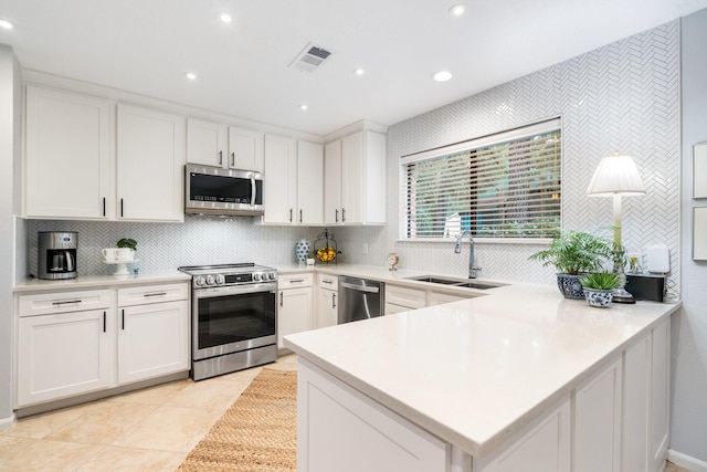 291 E Rainbow Ridge Cir, The Woodlands, TX 77381 - kitchen with stainless steel appliances, backsplash, a peninsula, white cabinetry, and light countertops