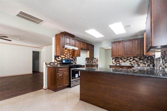 5402 Sheraton Oaks Dr, Houston, TX 77091 - kitchen with stainless steel range with gas cooktop, under cabinet range hood, decorative backsplash, a peninsula, and dark stone countertops