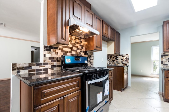 5402 Sheraton Oaks Dr, Houston, TX 77091 - kitchen with stainless steel gas range, under cabinet range hood, tasteful backsplash, dark stone countertops, and light tile patterned flooring