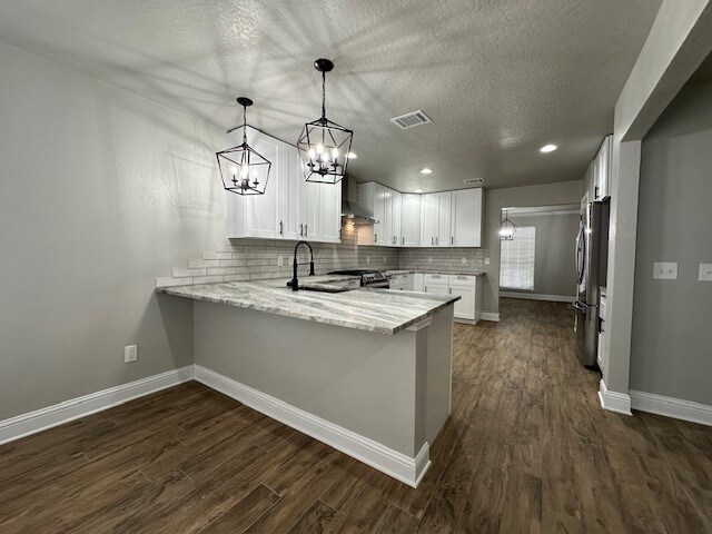 2102 Autumn Cove Dr, League City, TX 77573 - kitchen featuring appliances with stainless steel finishes, a peninsula, light stone countertops, dark wood-style floors, and decorative backsplash
