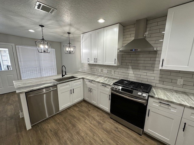 2102 Autumn Cove Dr, League City, TX 77573 - kitchen featuring wall chimney exhaust hood, appliances with stainless steel finishes, a peninsula, white cabinets, and a textured ceiling