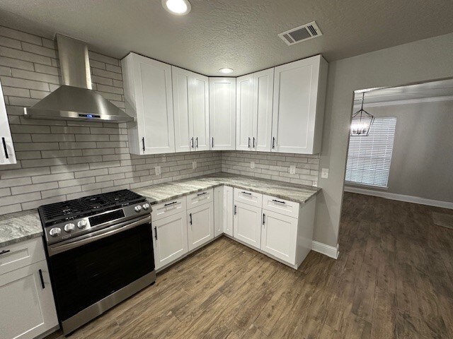 2102 Autumn Cove Dr, League City, TX 77573 - kitchen with wall chimney exhaust hood, stainless steel gas range, white cabinetry, dark wood-style flooring, and a textured ceiling