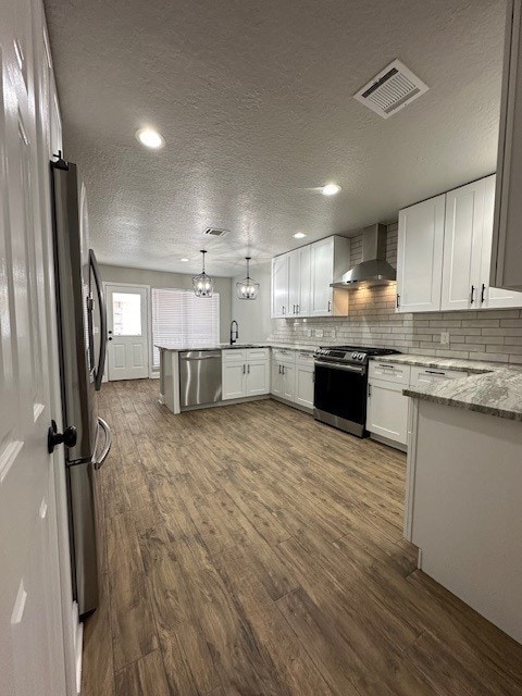 2102 Autumn Cove Dr, League City, TX 77573 - kitchen with wall chimney range hood, appliances with stainless steel finishes, a peninsula, a textured ceiling, and dark wood-type flooring