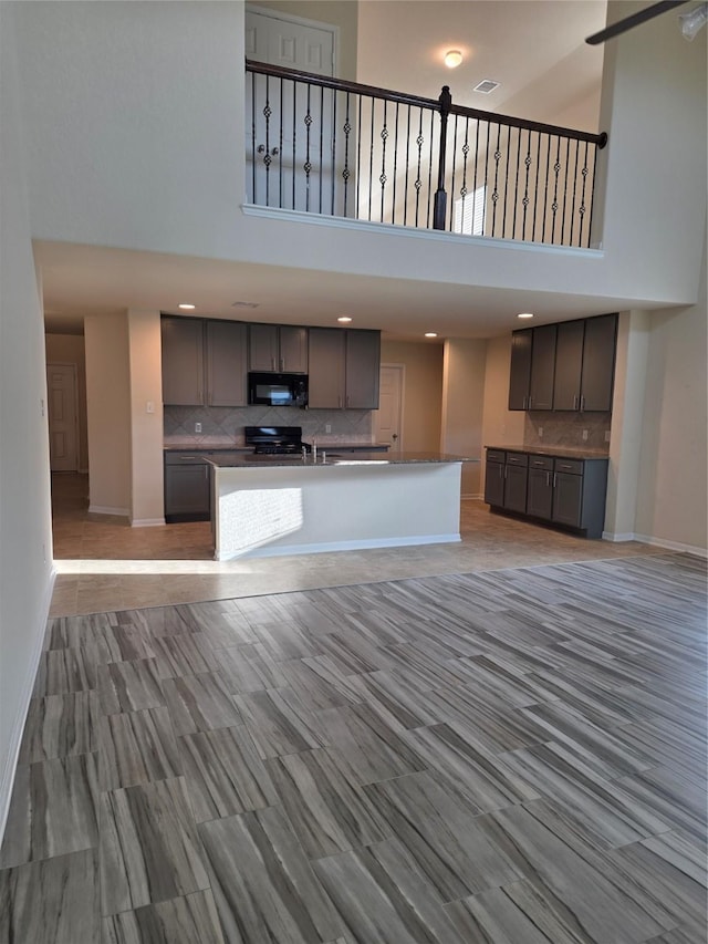 15319 Roaming River Trl, Houston, TX 77044 - kitchen with black microwave, a high ceiling, gray cabinets, backsplash, and range