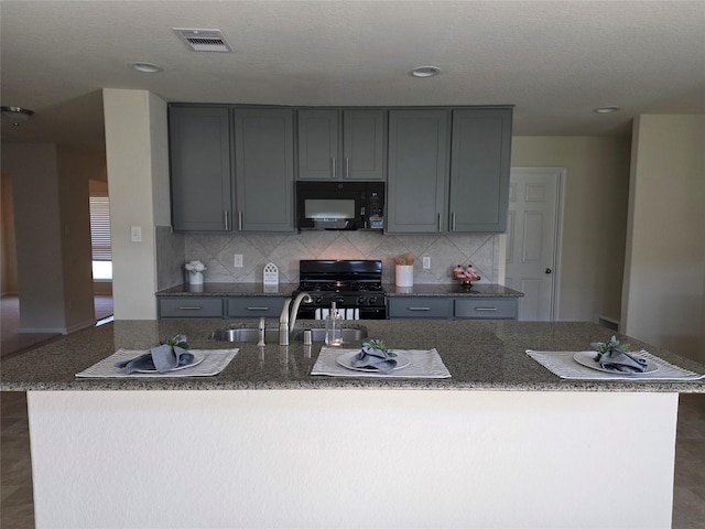 15319 Roaming River Trl, Houston, TX 77044 - kitchen with black appliances, gray cabinetry, decorative backsplash, an island with sink, and dark stone counters