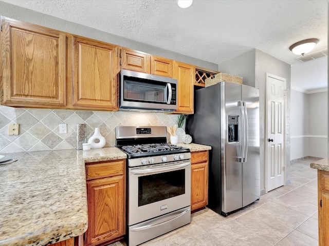 1227 Redwood Bough Ln, Houston, TX 77062 - kitchen featuring stainless steel appliances, backsplash, a textured ceiling, light tile patterned floors, and light stone countertops
