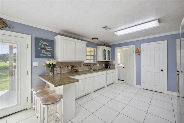11156 Country Ln, Beaumont, TX 77705 - kitchen with white cabinets, a breakfast bar, ornamental molding, a textured ceiling, and glass insert cabinets