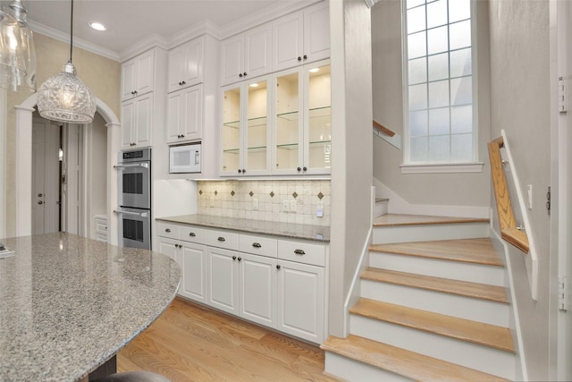 6616 Queensclub Dr, Houston, TX 77069 - kitchen featuring stainless steel double oven, white microwave, light wood-style floors, decorative backsplash, and crown molding