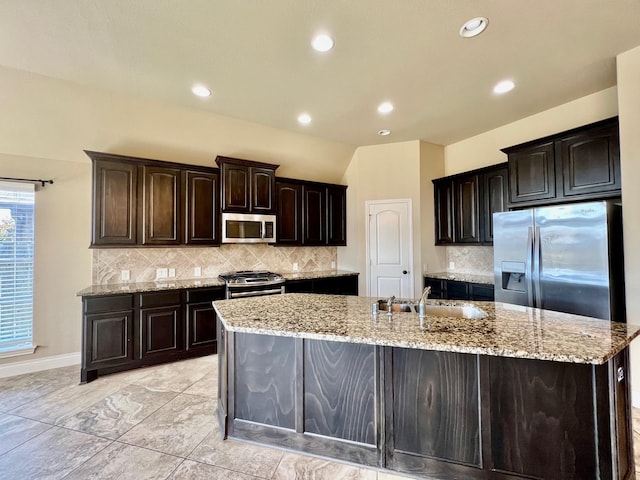 22223 Slate Oaks Ln, Richmond, TX 77469 - kitchen featuring appliances with stainless steel finishes, a kitchen island with sink, decorative backsplash, light stone counters, and recessed lighting
