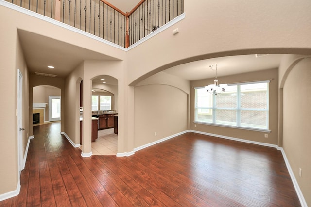 30041 Willow Walk Ln, Brookshire, TX 77423 - unfurnished living room featuring dark wood finished floors, arched walkways, a chandelier, a tiled fireplace, and a towering ceiling