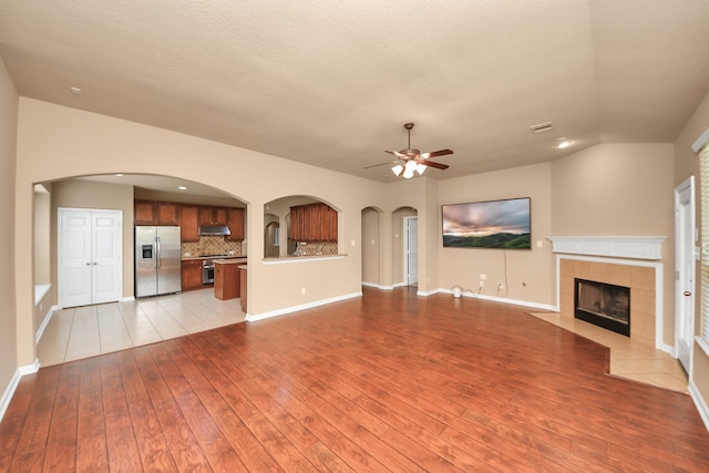 30041 Willow Walk Ln, Brookshire, TX 77423 - unfurnished living room with a tiled fireplace, ceiling fan, light wood-style flooring, lofted ceiling, and arched walkways