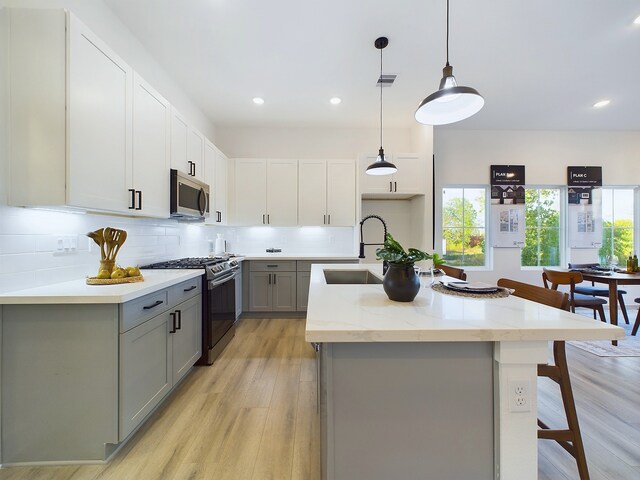 2704 Jensen Creek Ln, Houston, TX 77026 - kitchen featuring appliances with stainless steel finishes, gray cabinetry, light wood-style floors, a kitchen island with sink, and tasteful backsplash