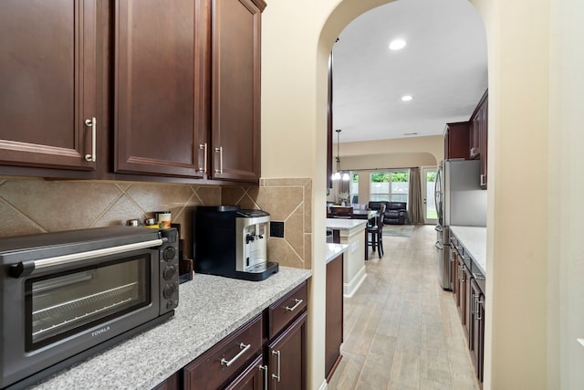 10522 Ginger Gln, Missouri City, TX 77459 - kitchen featuring light wood-style floors, arched walkways, backsplash, recessed lighting, and light stone countertops