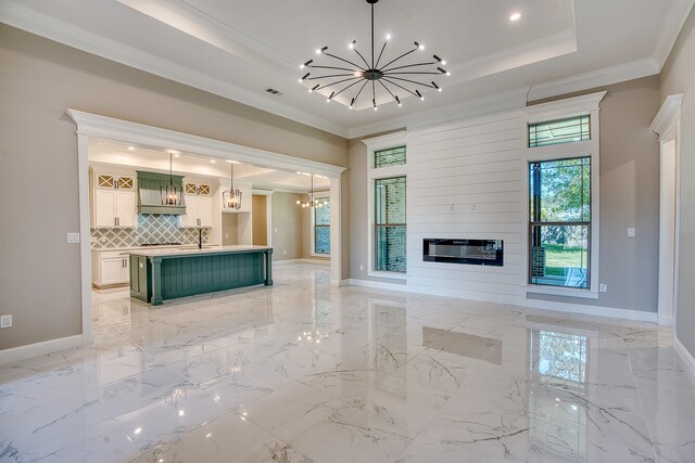 255 W Caldwood Dr, Beaumont, TX 77707 - unfurnished living room with a chandelier, ornamental molding, a tray ceiling, a large fireplace, and light marble finish floors