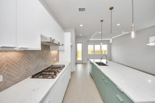 3003A Ventas Dr, Houston, TX 77047 - kitchen with stainless steel gas cooktop, under cabinet range hood, tasteful backsplash, white cabinetry, and green cabinetry