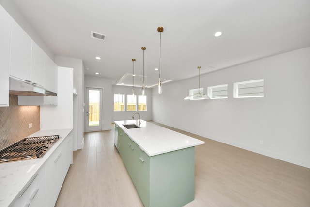 3003A Ventas Dr, Houston, TX 77047 - kitchen with stainless steel gas cooktop, light wood-style flooring, white cabinets, tasteful backsplash, and a center island with sink