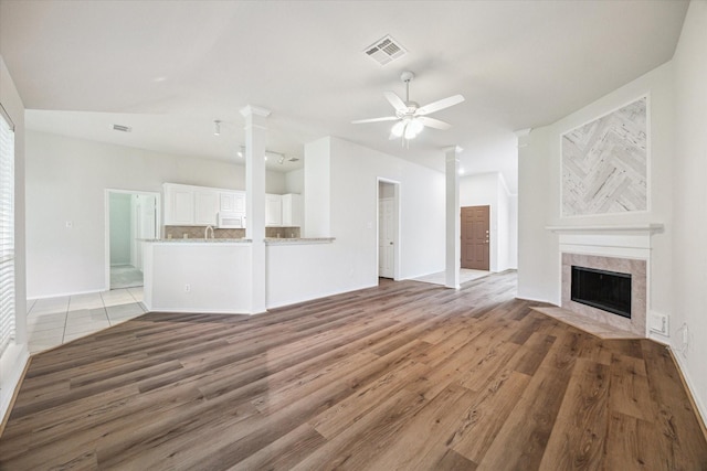 8211 Broken Timber Way, Houston, TX 77095 - unfurnished living room featuring ceiling fan, a tile fireplace, light wood-style flooring, and decorative columns