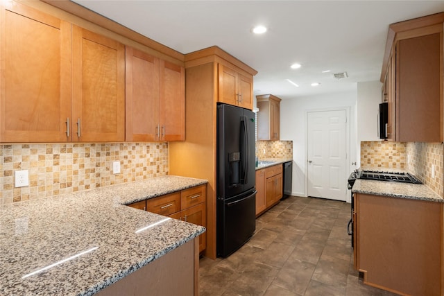 217 Wellwood Ln, Conroe, TX 77304 - kitchen featuring black refrigerator with ice dispenser, decorative backsplash, light stone countertops, recessed lighting, and stainless steel microwave