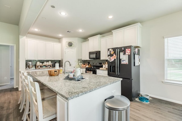 2337 Shalmar Dr, West Columbia, TX 77486 - kitchen featuring black appliances, decorative backsplash, wood finished floors, a kitchen bar, and recessed lighting