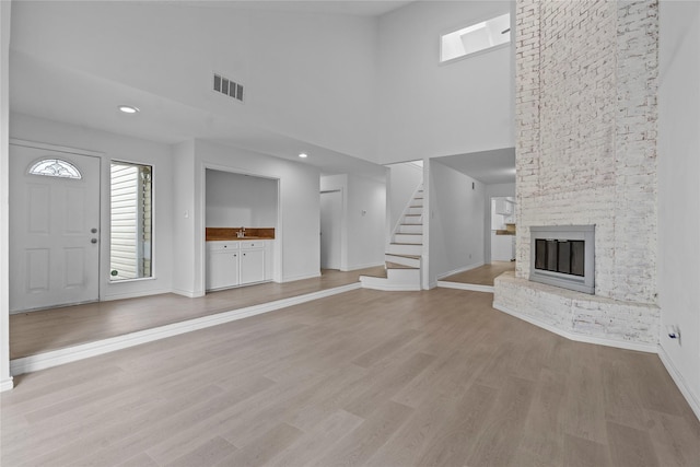 11011 Bandlon Dr, Houston, TX 77072 - unfurnished living room featuring a towering ceiling, a large fireplace, stairway, light wood-style floors, and recessed lighting