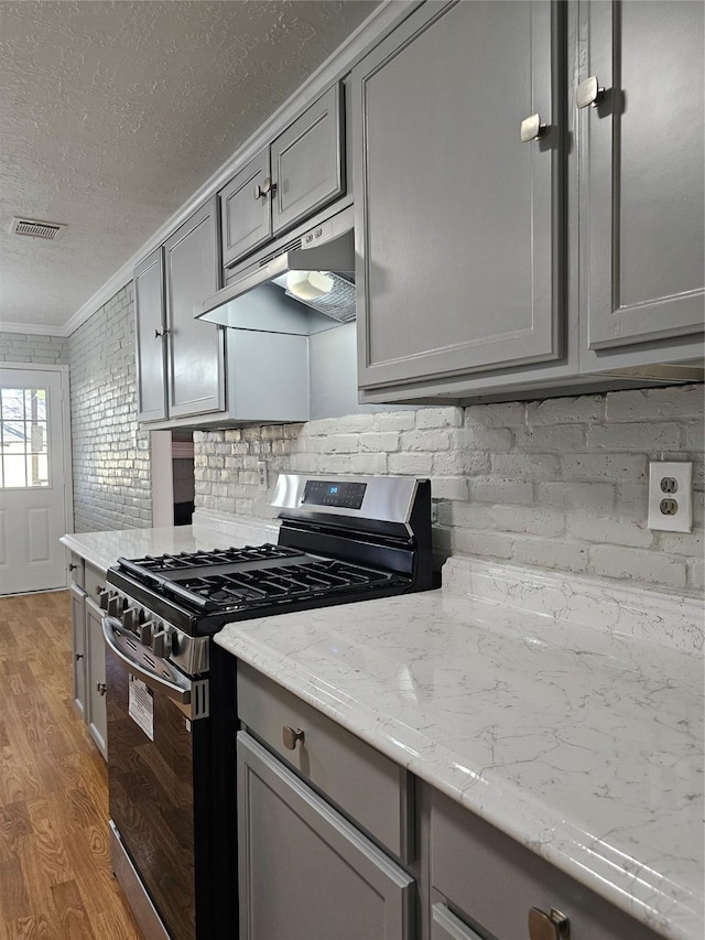 7715 Lobera Dr, Houston, TX 77083 - kitchen featuring stainless steel gas range oven, under cabinet range hood, gray cabinetry, light wood-type flooring, and a textured ceiling