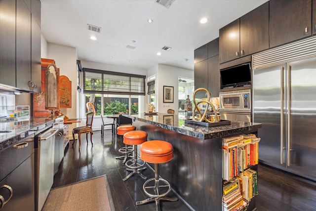 2409 Maconda Ln, Houston, TX 77027 - kitchen featuring built in appliances, dark wood-style flooring, a kitchen bar, dark stone counters, and a kitchen island