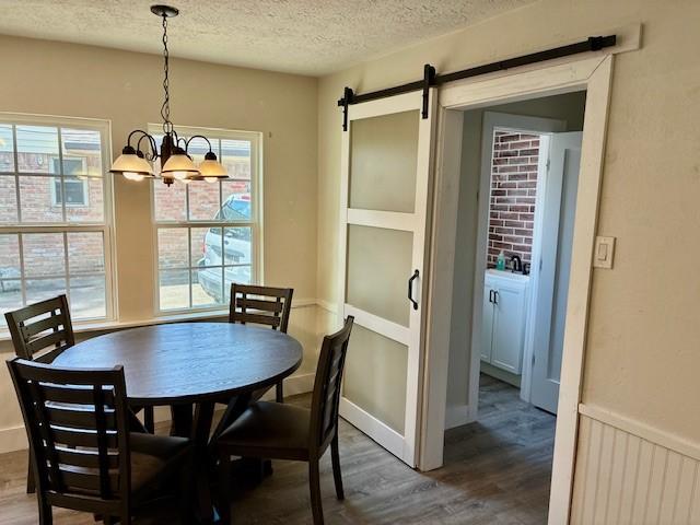 29019 Elmwood Dr, Shenandoah, TX 77381 - dining space featuring wood finished floors, a textured ceiling, a chandelier, and a barn door