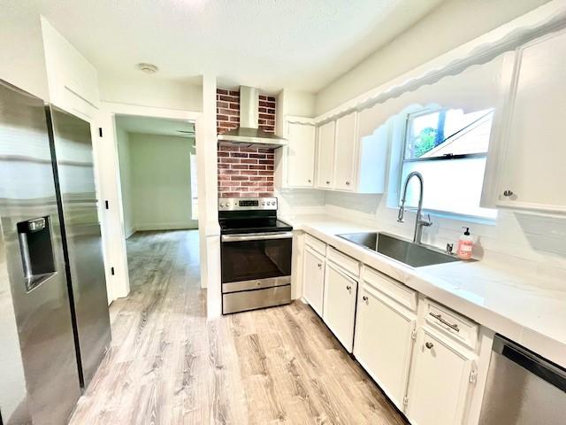 29019 Elmwood Dr, Shenandoah, TX 77381 - kitchen with stainless steel appliances, wall chimney exhaust hood, white cabinetry, light wood-type flooring, and light countertops