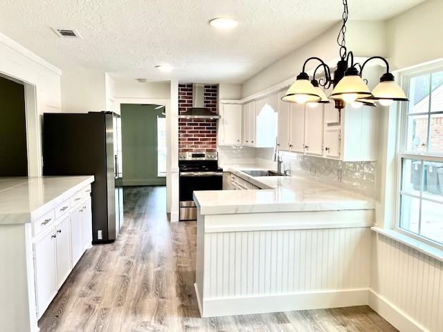 29019 Elmwood Dr, Shenandoah, TX 77381 - kitchen featuring appliances with stainless steel finishes, wall chimney exhaust hood, a peninsula, a chandelier, and light wood-type flooring