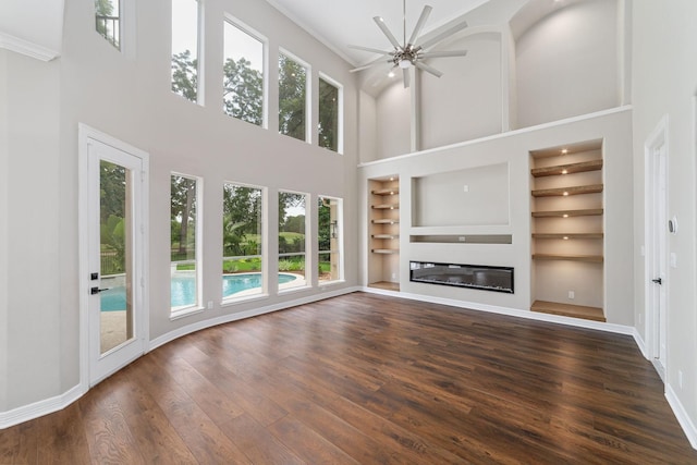 18 Sullivans Ct, Missouri City, TX 77459 - unfurnished living room featuring a high ceiling, built in features, a glass covered fireplace, dark wood finished floors, and ceiling fan