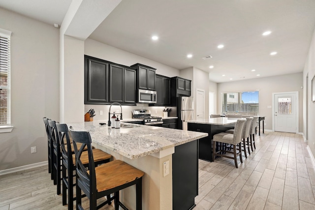 31230 Pinebrook Falls Ln SE, Hockley, TX 77447 - kitchen with appliances with stainless steel finishes, dark cabinetry, light wood-style floors, a breakfast bar, and a kitchen island