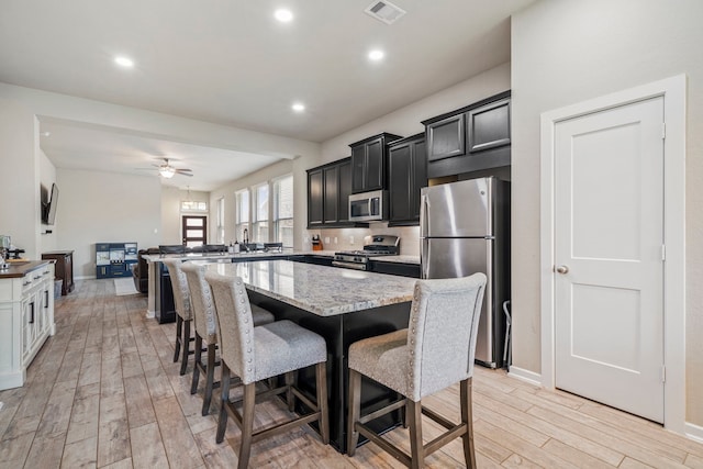 31230 Pinebrook Falls Ln SE, Hockley, TX 77447 - kitchen featuring stainless steel appliances, light wood-style flooring, a kitchen breakfast bar, a ceiling fan, and dark cabinets