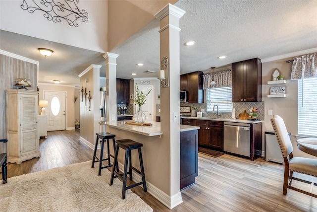 11823 Solon Springs Dr, Tomball, TX 77375 - kitchen featuring stainless steel appliances, ornate columns, dark brown cabinetry, a breakfast bar area, and light wood-type flooring