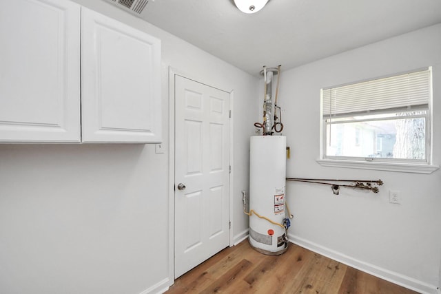 9250 Wiloak St, Houston, TX 77028 - laundry area featuring gas water heater, wood finished floors, and cabinet space