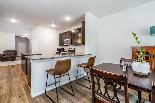 1166 Magnolia Branch Ln, Tomball, TX 77375 - kitchen with stainless steel microwave, dark stone countertops, light wood-type flooring, backsplash, and a peninsula