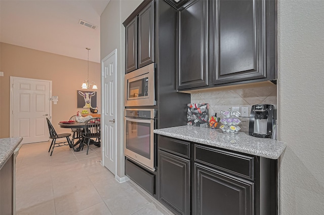 9107 Solvista Pass Ln, Houston, TX 77070 - kitchen featuring appliances with stainless steel finishes, dark cabinets, decorative backsplash, light tile patterned flooring, and hanging light fixtures