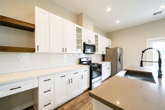 11325 Stonework Garden Ln, Houston, TX 77076 - kitchen featuring appliances with stainless steel finishes, backsplash, light wood finished floors, open shelves, and white cabinetry