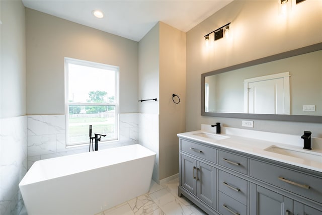 11325 Stonework Garden Ln, Houston, TX 77076 - bathroom with marble look tiles, tile walls, a freestanding tub, double vanity, and a wainscoted wall