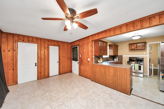418 Forrest St, Baytown, TX 77520 - kitchen featuring stainless steel gas stove, a ceiling fan, wooden walls, a peninsula, and brown cabinetry