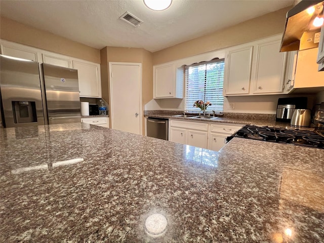 18738 Shannon Glen Ln, Houston, TX 77084 - kitchen featuring appliances with stainless steel finishes, exhaust hood, white cabinetry, and dark stone countertops